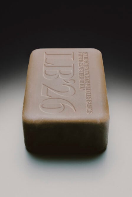 Handmade soap bar with embossed logo on top, natural beige color, rounded edges, studio shot on neutral background
