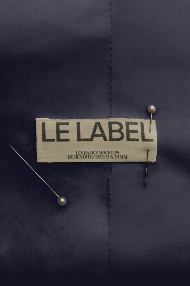 Cream woven label pinned on dark fabric with pearl-headed pins, showing "Le Label" text