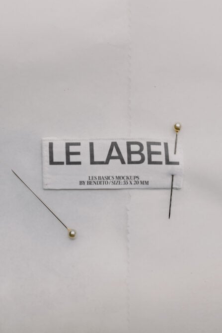 Woven clothing label mockup with gold sewing pins on white background