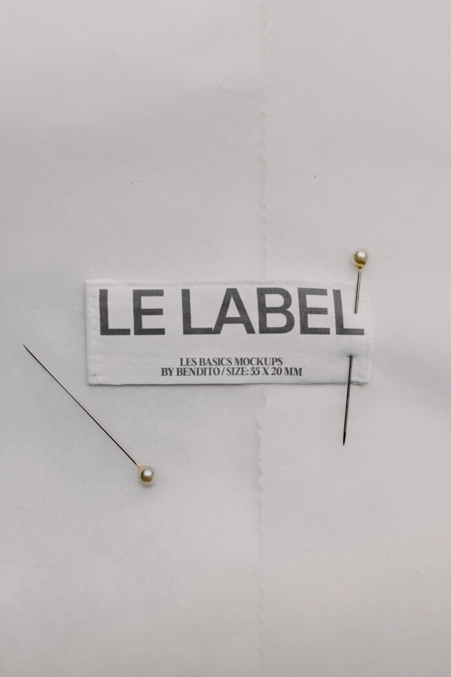 Woven clothing label mockup with gold sewing pins on white background