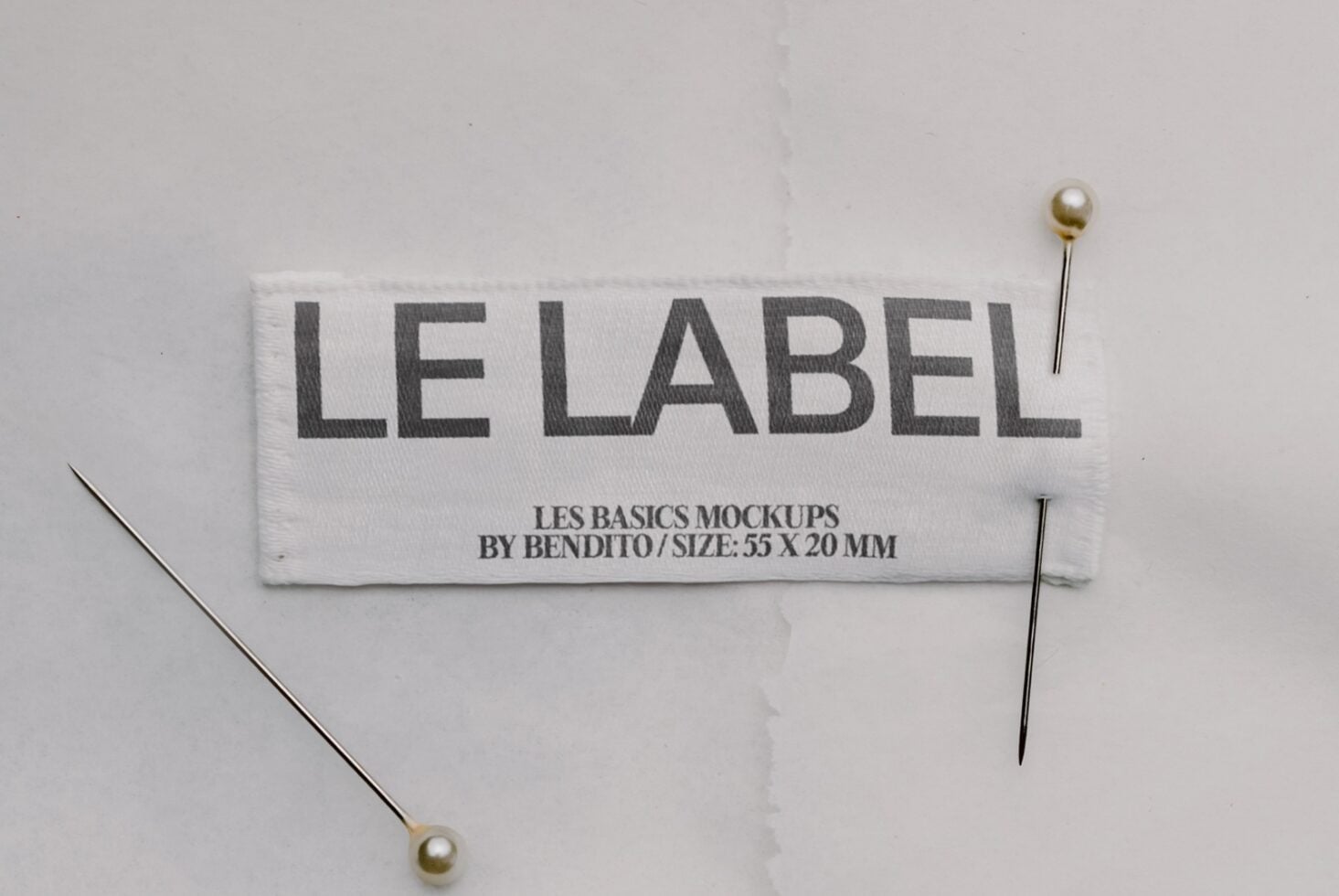Woven label mockup with "LE LABEL" text, pinned down with pearl-headed pins on white background
