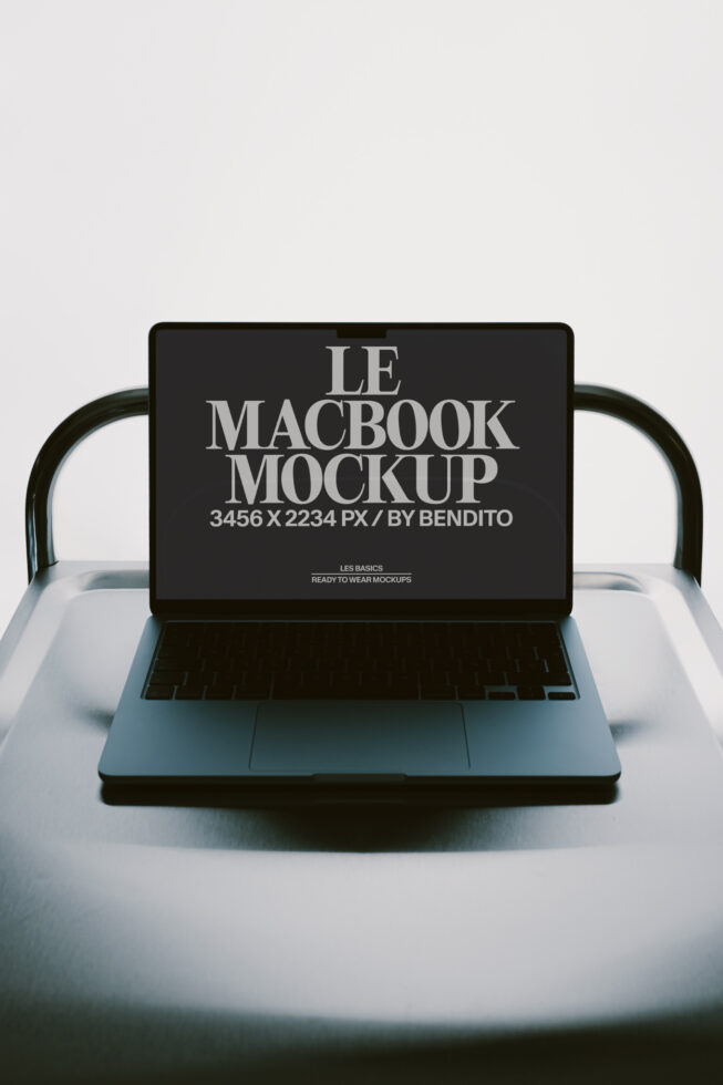 MacBook laptop mockup on white chair with black screen displaying serif typography