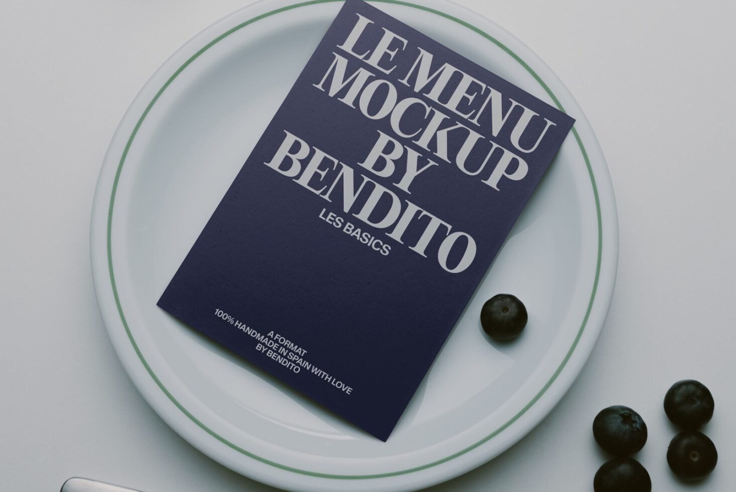 Navy book mockup on white plate with green rim, olives scattered beside