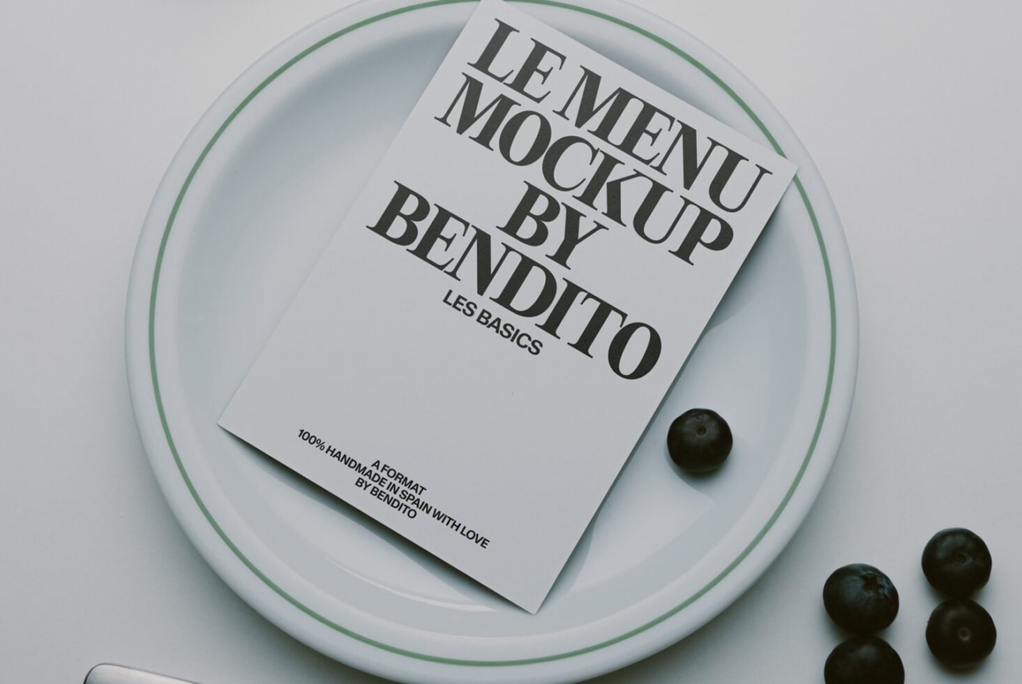 Minimalist magazine mockup on white plate with green rim, styled with olives
