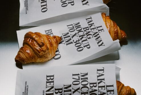Stacked paper bags with bold serif typography next to golden croissants casting shadows