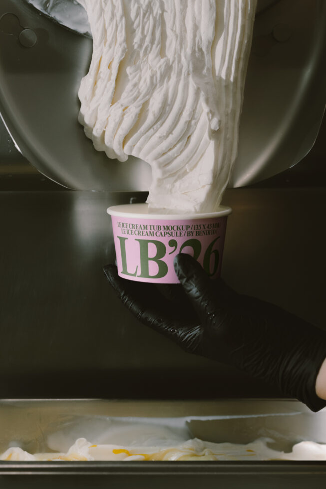 Whipped cream pouring into pink ice cream tub mockup with black gloved hands