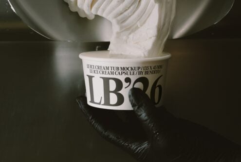 Ice cream tub mockup with whipped cream swirl, labeled LB'26, held in black gloved hands