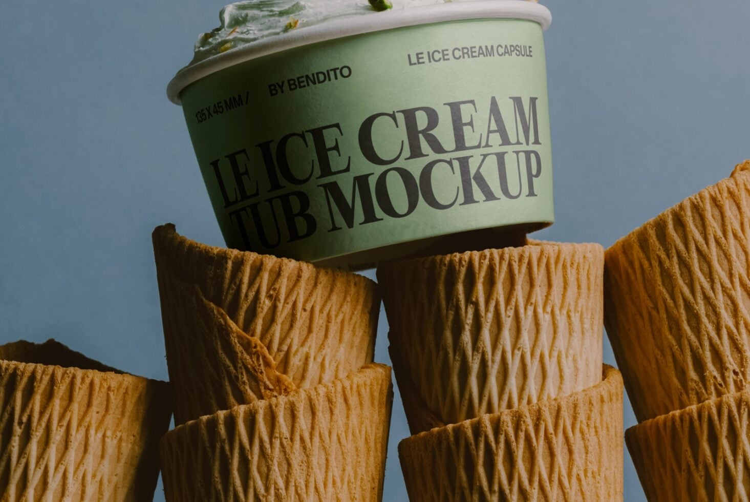 Mint green ice cream tub mockup sitting on waffle cone pieces against blue background