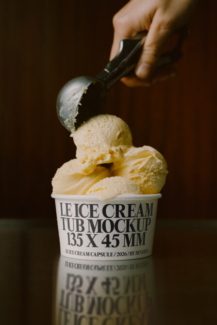 Vanilla ice cream scoop dripping into labeled cup on dark background with hand holding scoop