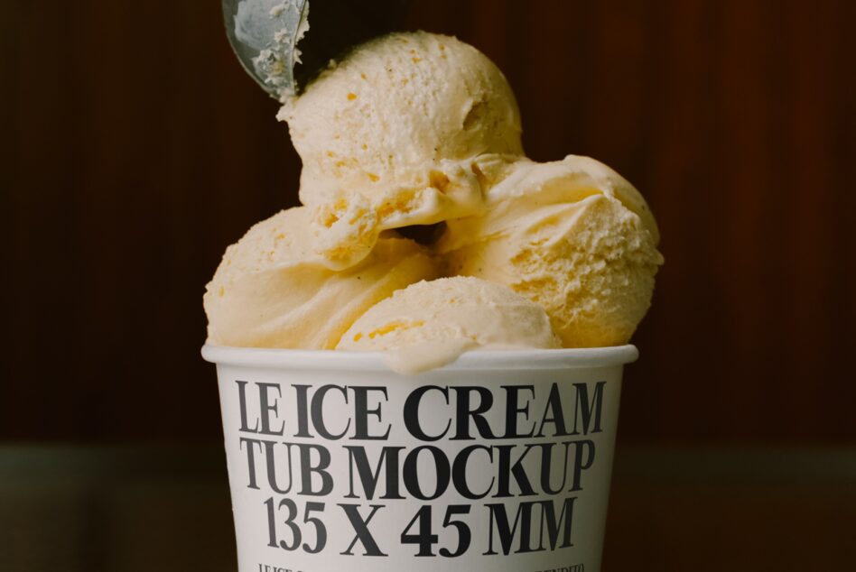 Vanilla ice cream scoops in white paper cup with spoon on dark background