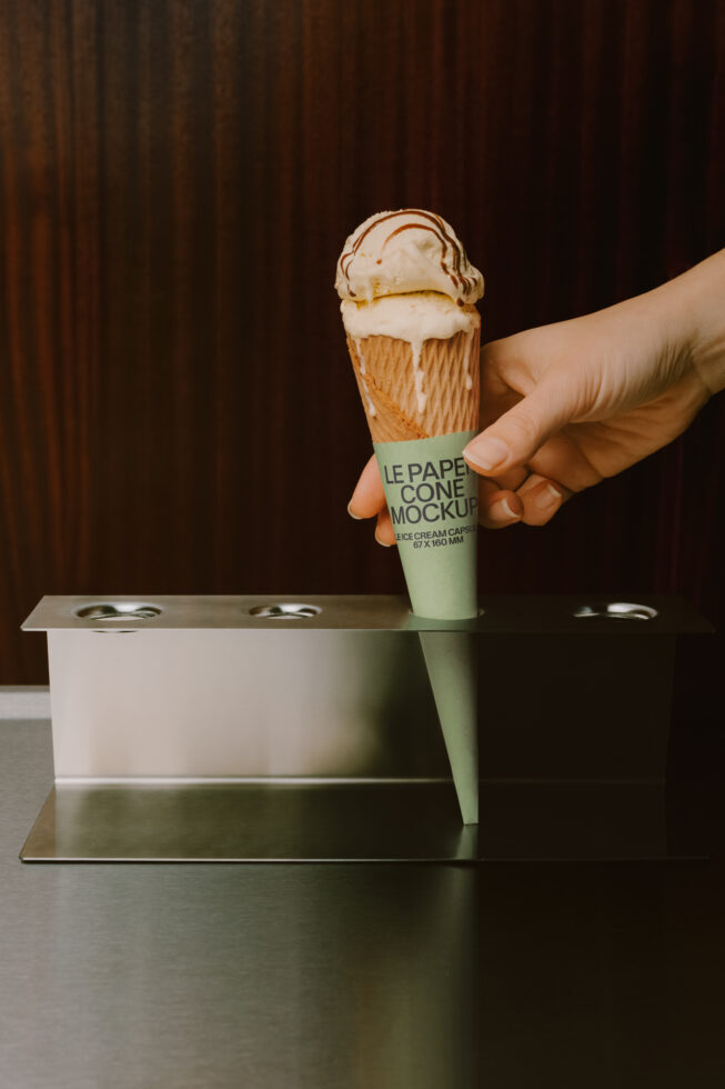 Hand holding ice cream cone with mint green paper wrapper label mockup against dark backdrop
