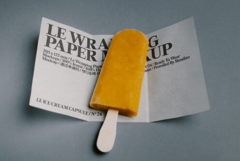 Yellow popsicle sitting on open wrapped paper mockup with multilingual text
