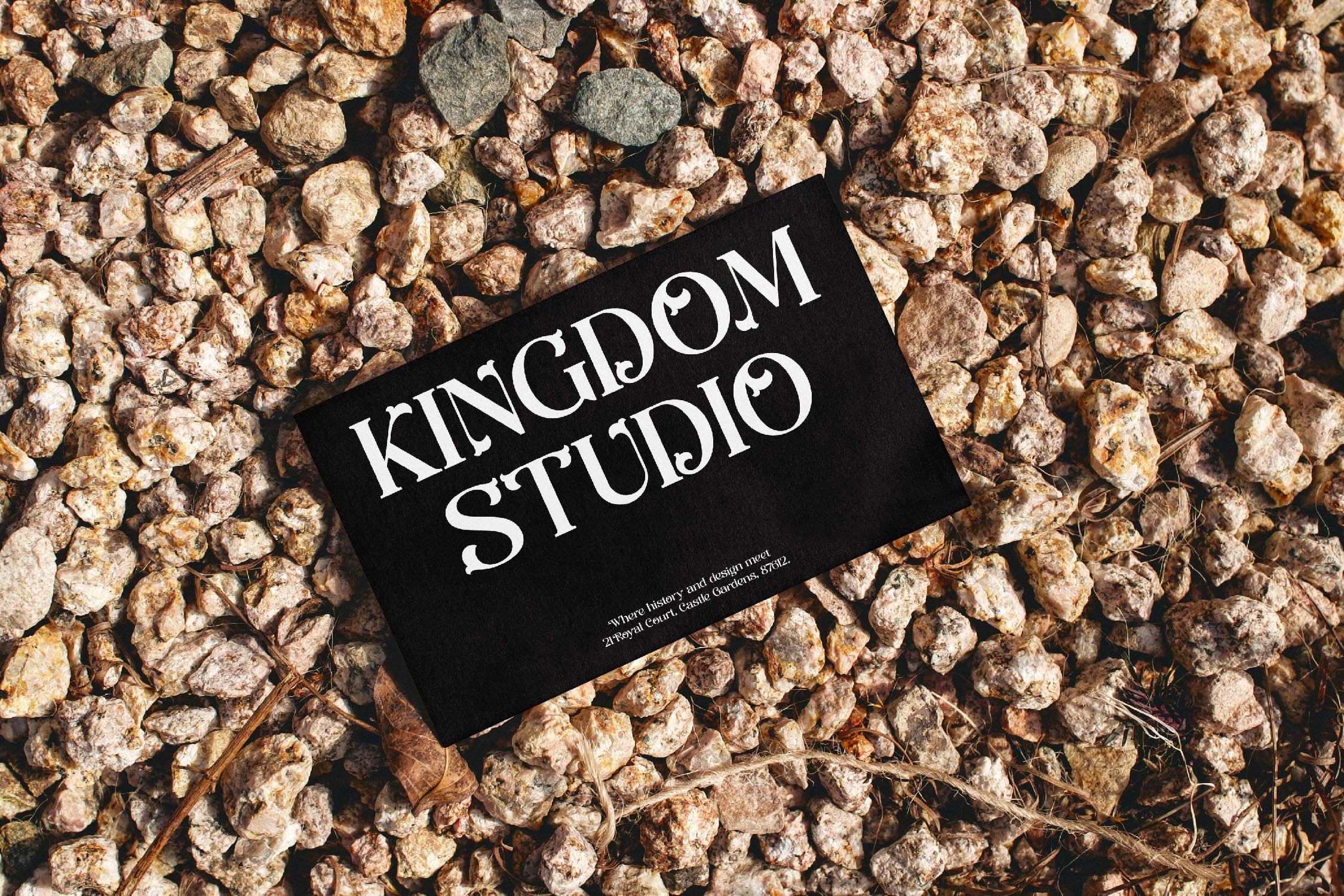 Black business card with "Kingdom Studio" serif typography laying on tan gravel surface