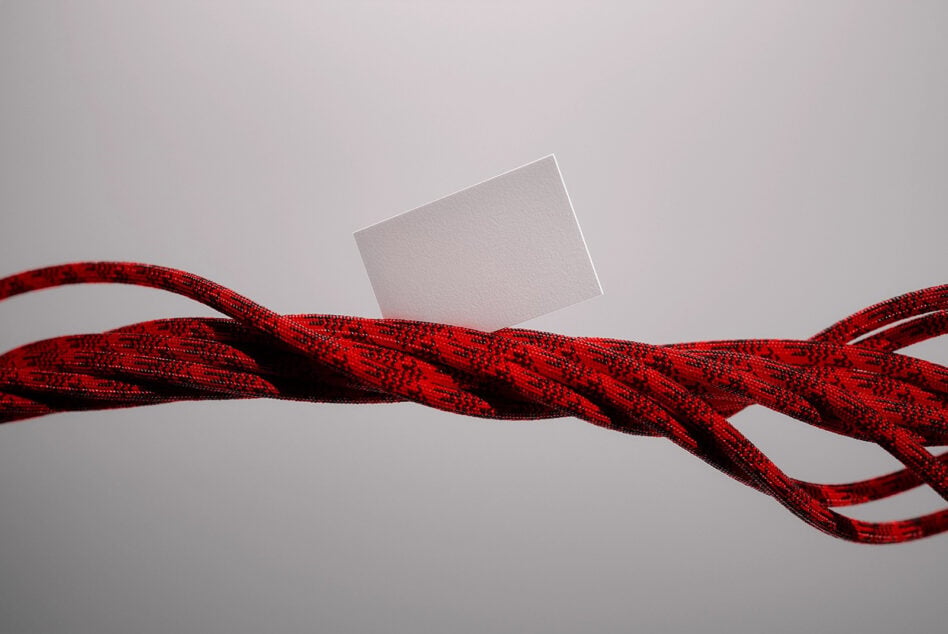 Blank business card floating above twisted red rope on neutral background