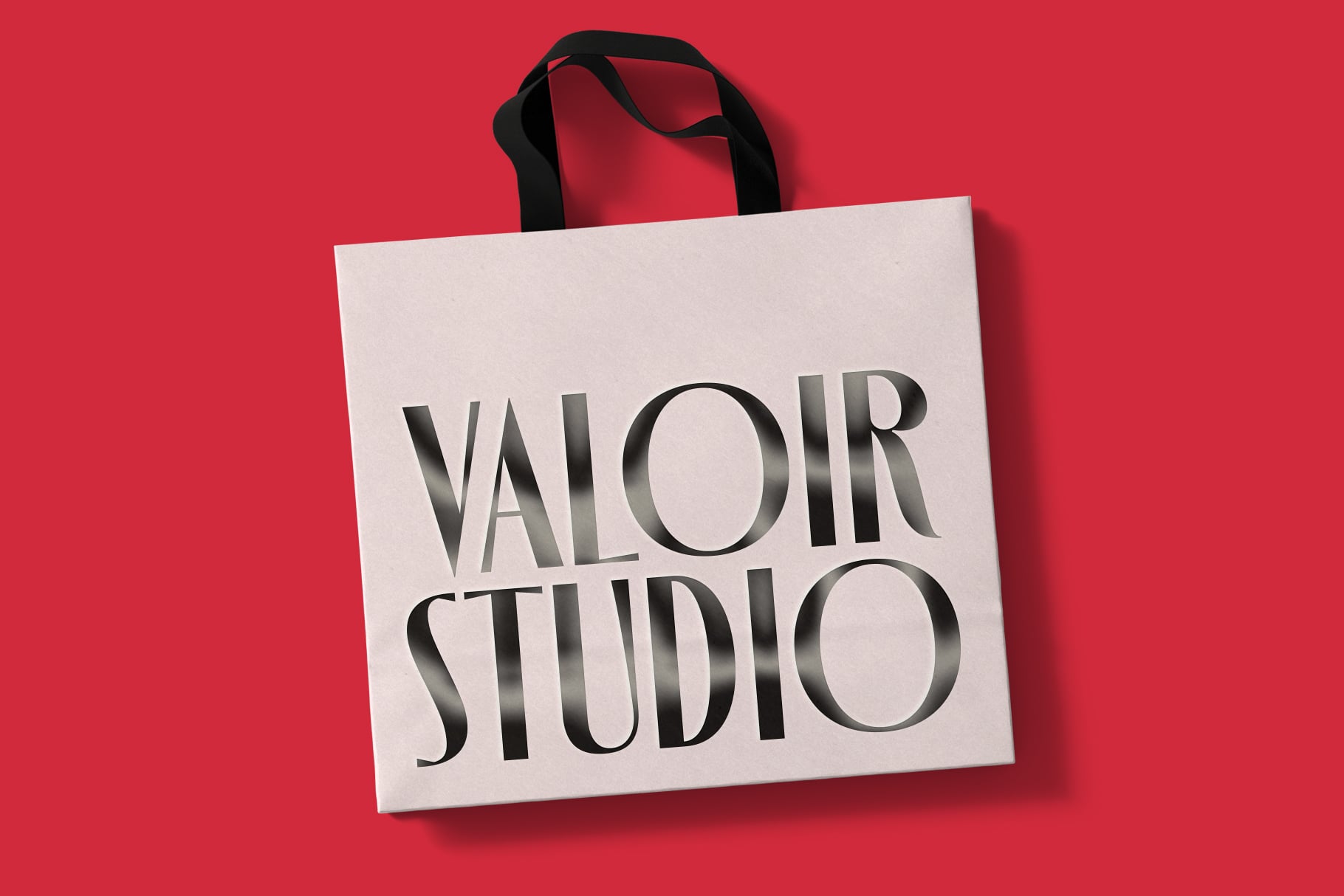 Canvas tote bag mockup with black handles on bright red background showing Valoir Studio branding