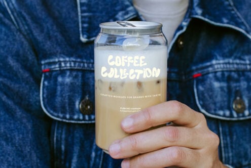 Hand holding iced coffee jar mockup with custom label on denim background