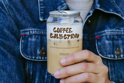 Hand holding iced coffee jar mockup with brown lettering on denim jacket background