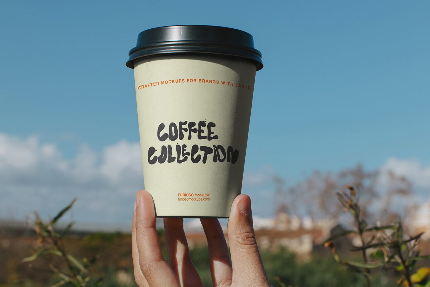 Coffee cup mockup held up to bright sky with hand, black lid, cream sleeve with bold lettering