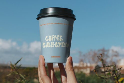 Coffee cup mockup held up to bright sky with cream colored branding text