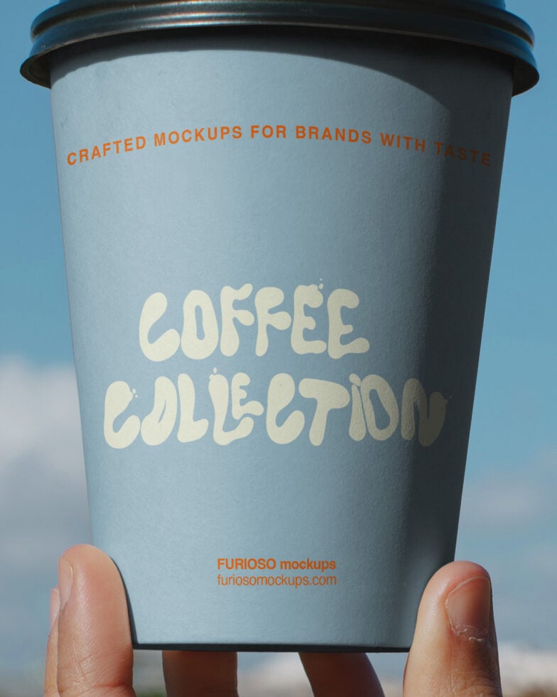 Coffee cup mockup held up to sky with cream colored text on blue cup