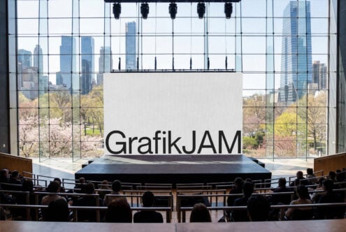 Modern auditorium stage with GrafikJAM sign, city skyline through floor-to-ceiling windows