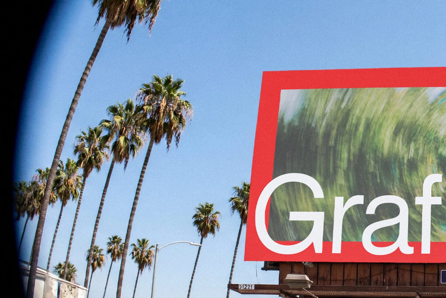 Sunny LA street with tall palm trees, clear blue sky, red billboard with white text on right side