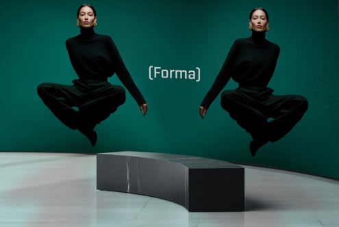 Two models in black turtlenecks jumping over curved marble bench against teal wall