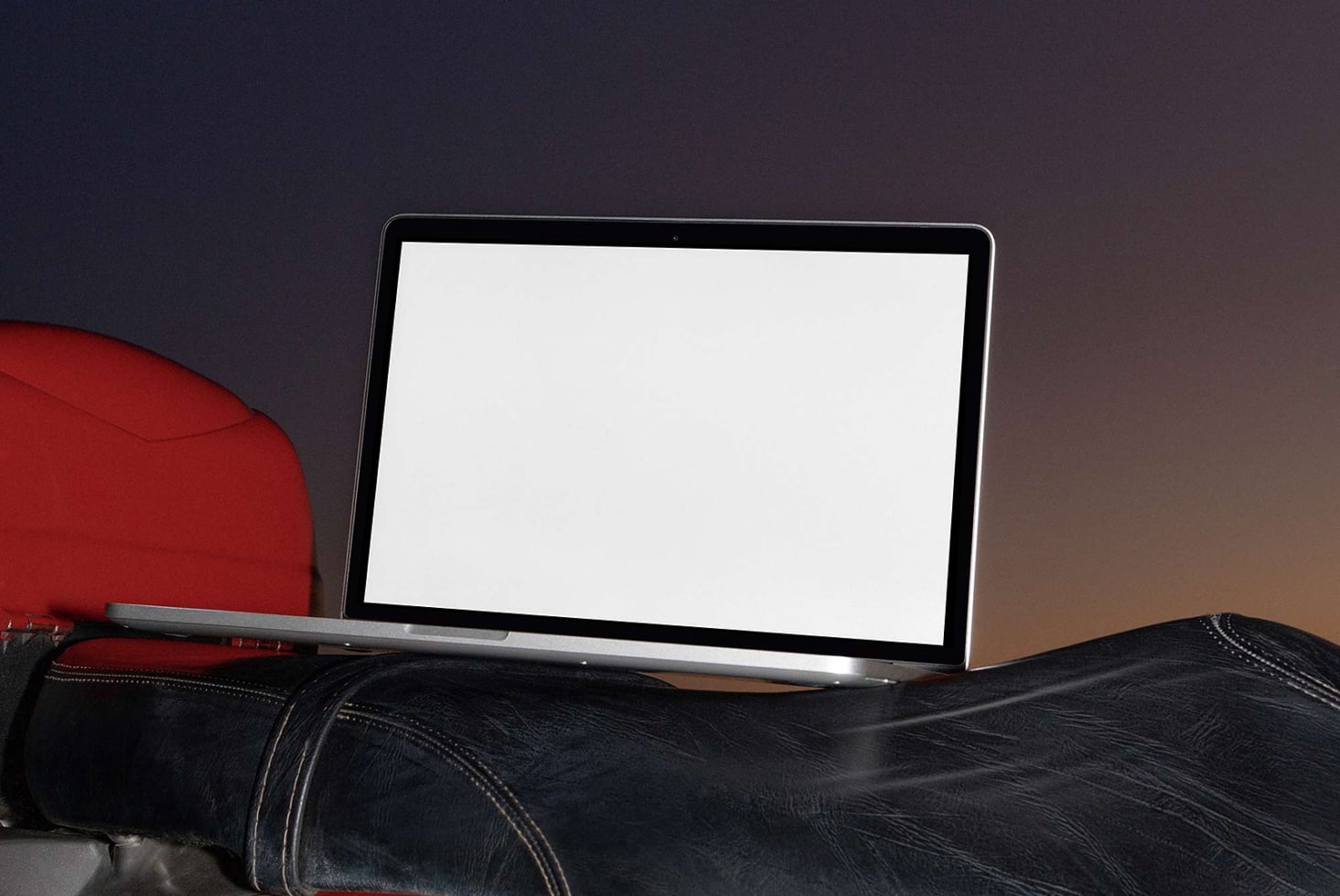 Laptop mockup on leather couch with red cushion, blank screen ready for design work