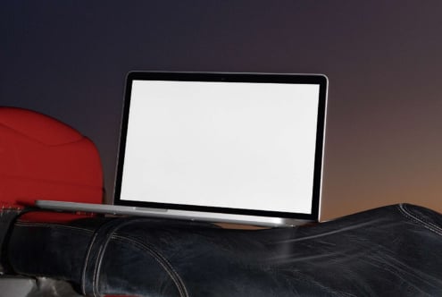 Laptop mockup on leather couch with red cushion, blank screen ready for design work