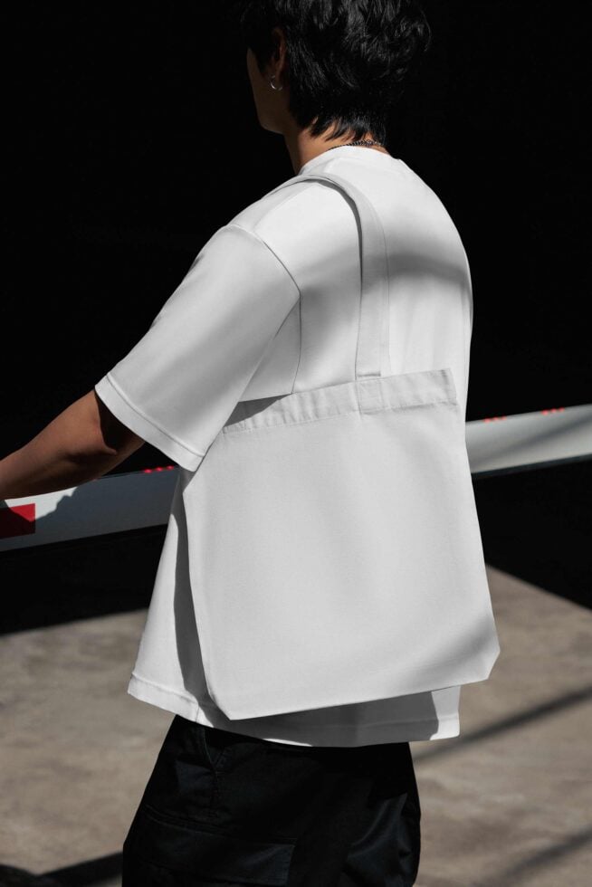 Woman wearing white oversized shirt over black pants, shot from behind against dark background