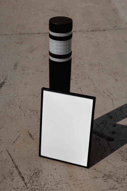 Black bollard with reflective tape next to blank sign mockup on concrete ground