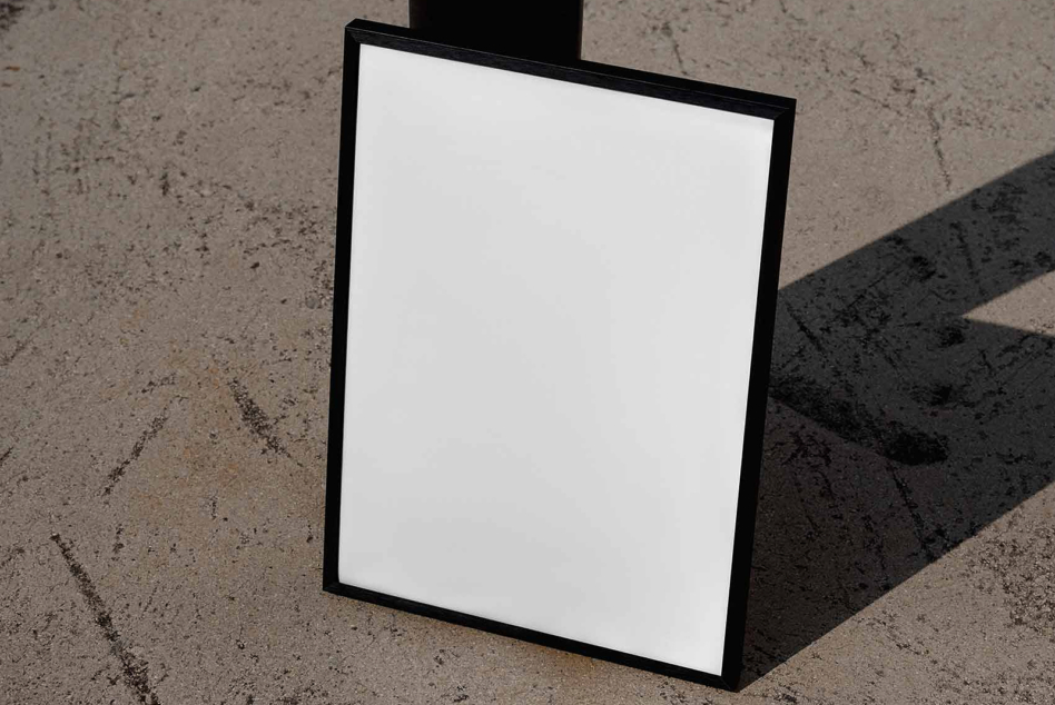 Black frame leaning on concrete with hard shadow, blank white space inside ready for your design