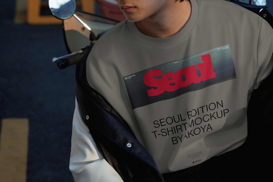 Person wearing cream tee with red Seoul graphic print, styled mockup shot in moody studio lighting