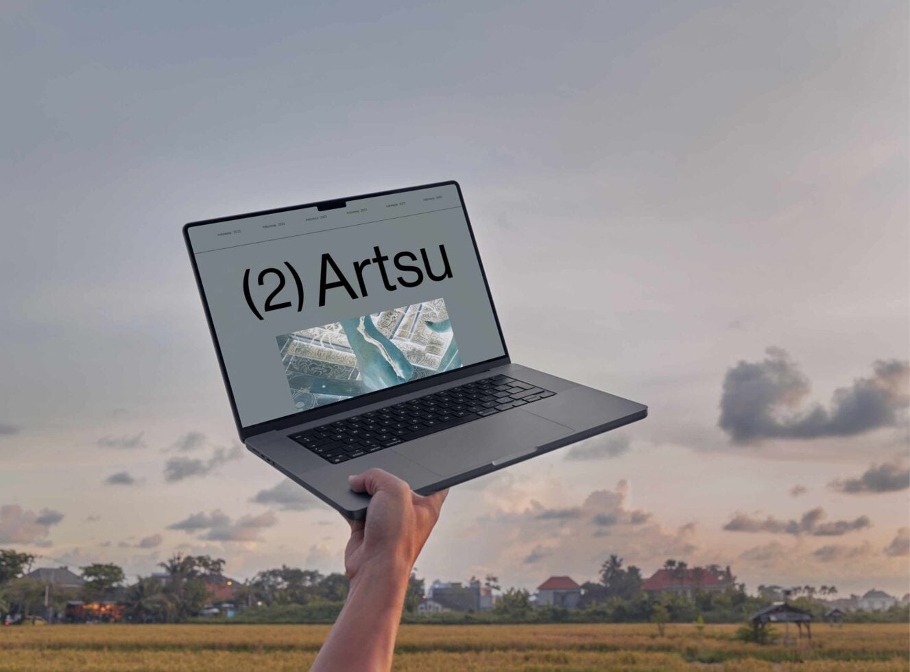 Laptop mockup held up against sunset sky showing Artsu branding with aerial imagery on screen