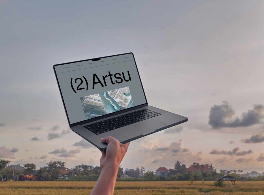 Laptop mockup held up against sunset sky showing Artsu branding with aerial imagery on screen