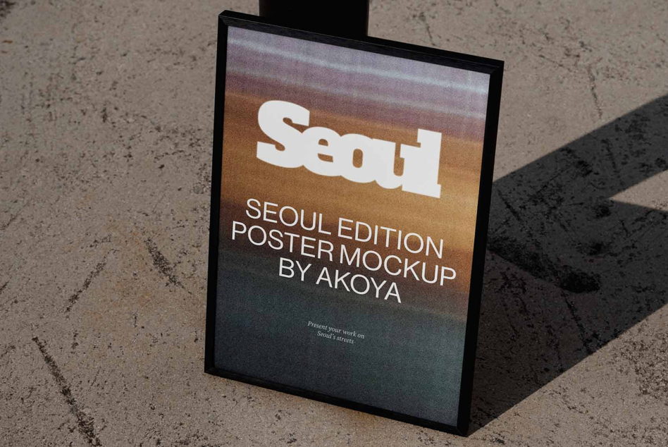 Framed poster mockup leaning on concrete with warm gradient background, Seoul branding displayed