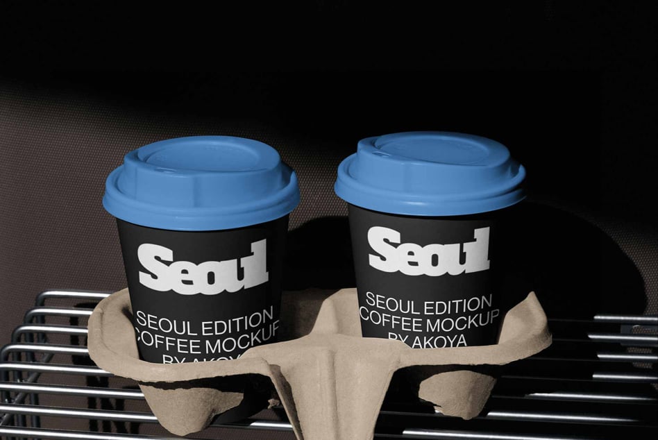 Two black coffee cups with blue lids in cardboard carrier on dark textured background