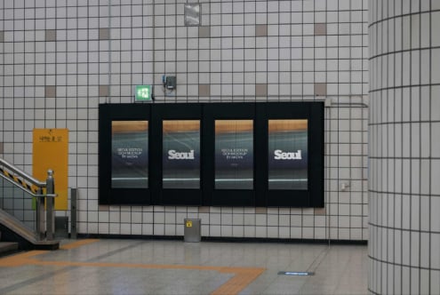 Four-panel subway poster mockup showing Seoul edition design with sunset imagery on tiled wall