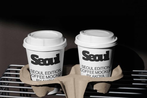 Two white coffee cups with Seoul branding sitting in cardboard carrier on dark textured background