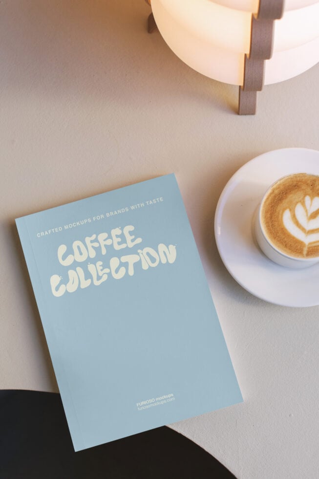 Flat lay of blue booklet next to latte with latte art, modern lamp casting shadows overhead