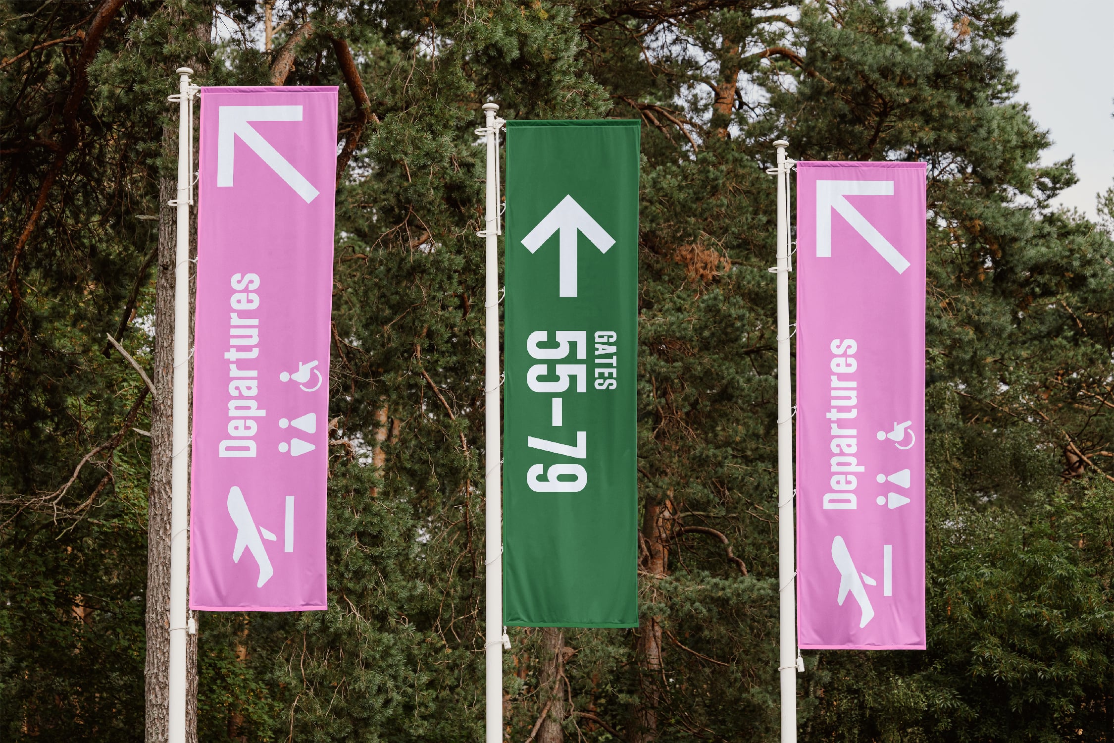 Outdoor banner mockup showing three vertical flags hanging on poles against pine trees