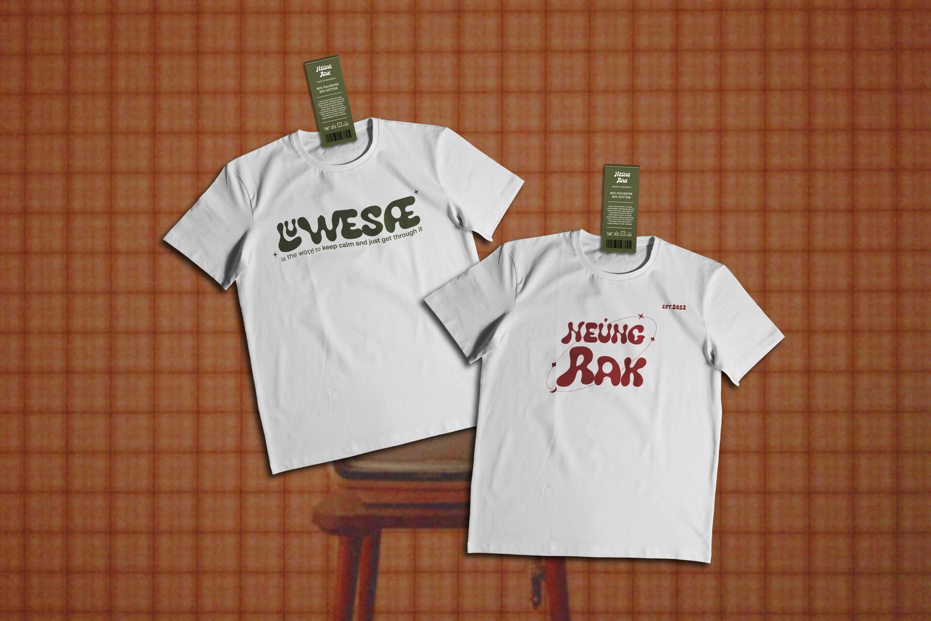 Two white tees with custom typography designs on terracotta grid backdrop with hang tags