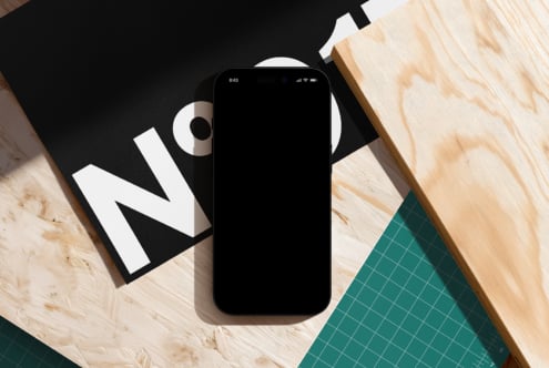Black phone on wood desk with design materials, geometric shapes, cool minimal setup shot