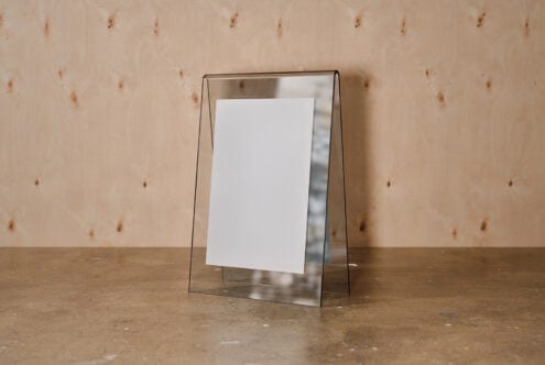 Clear acrylic frame with white card propped on concrete surface against textured plywood wall