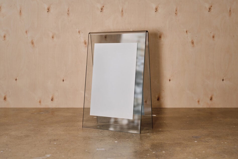 Clear acrylic frame with white card propped on concrete surface against textured plywood wall