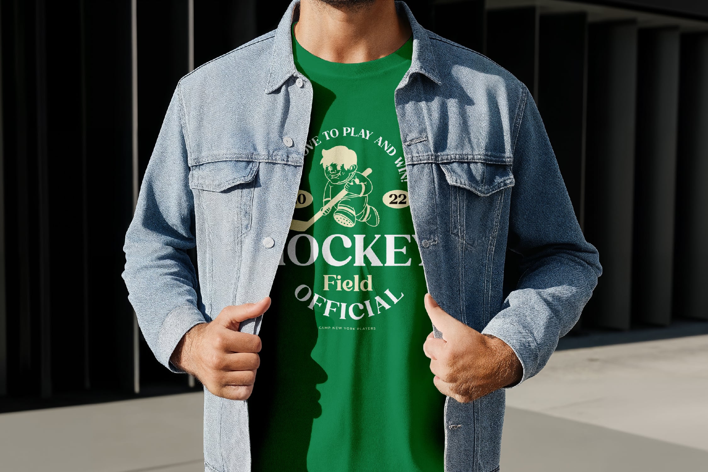 Guy wearing light wash denim jacket over green hockey graphic tee with vintage sports print
