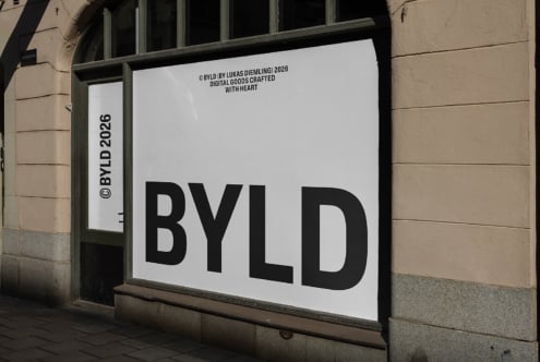Storefront window mockup showing BYLD branding on white poster with black typography, mounted in sage frame against stone building