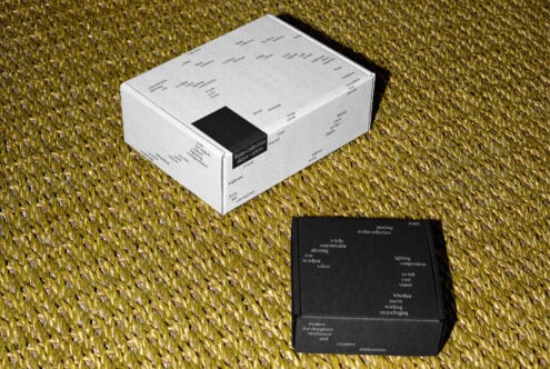 White box with black label detail shot next to open black box on textured yellow surface