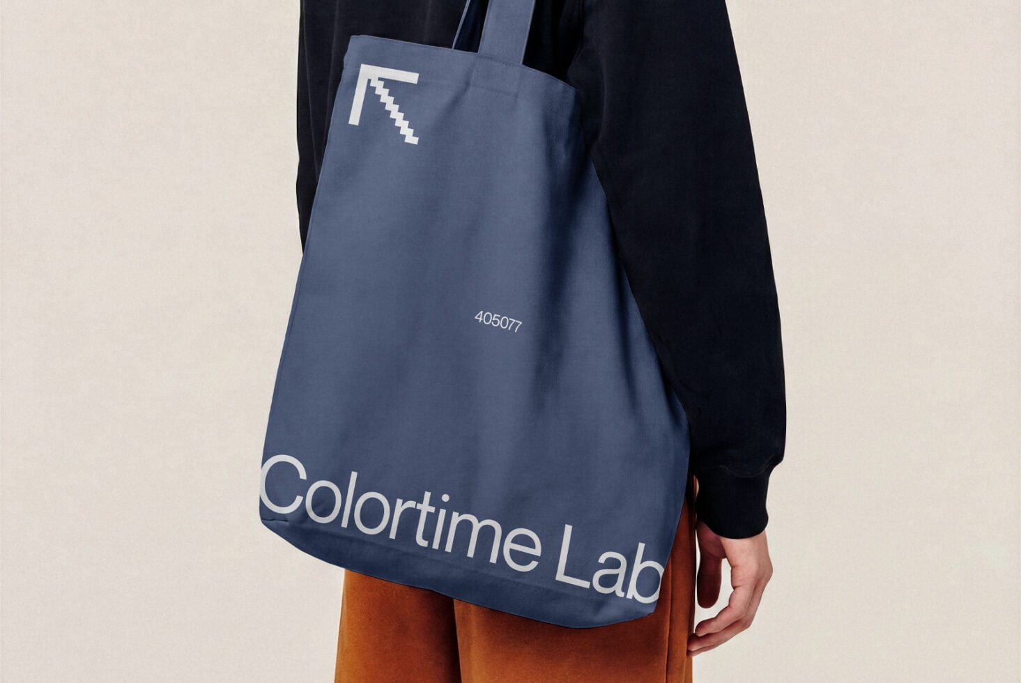 Blue tote bag mockup with pixel logo, worn over shoulder with navy jacket, orange pants visible