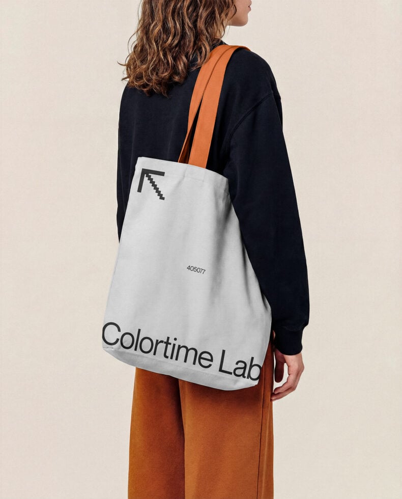 Woman wearing black sweatshirt with white tote bag slung over orange strap